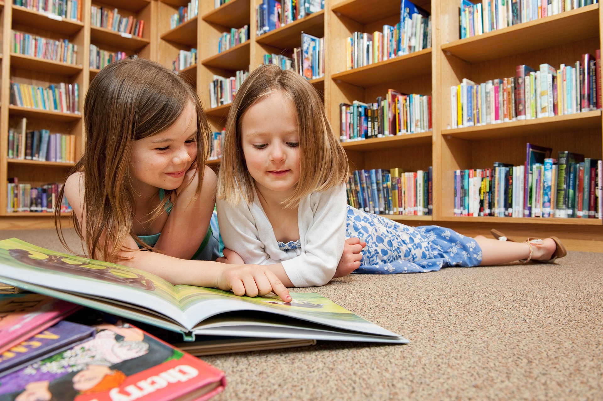 Two female children reading books in a library setting